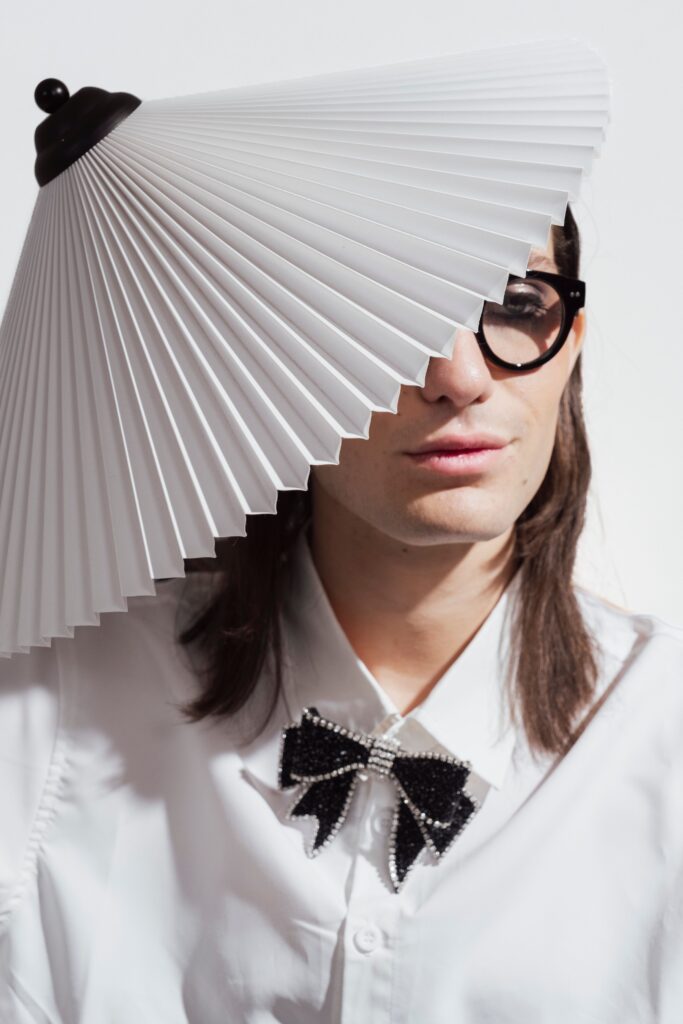 A stylish person in glasses with creative fashion sense, wearing a lampshade hat indoors.